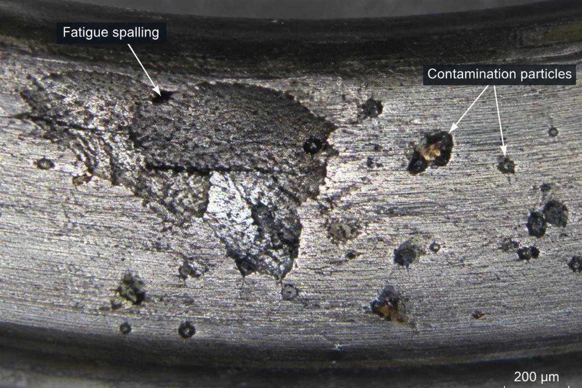 Microscopic view of bearing raceway showing fatigue spalling and contamination particles